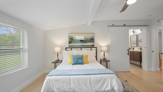 bedroom featuring ceiling fan, light hardwood / wood-style flooring, a barn door, connected bathroom, and lofted ceiling with beams