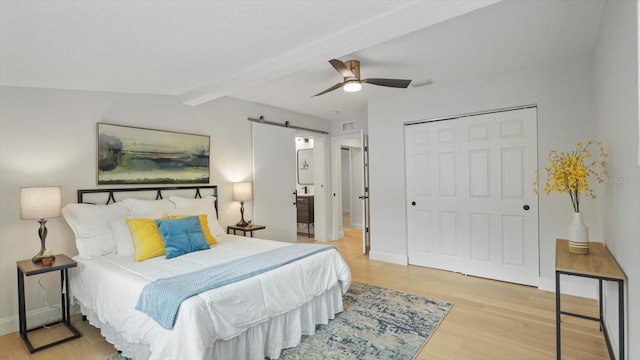 bedroom featuring beam ceiling, a closet, light hardwood / wood-style floors, ceiling fan, and a barn door