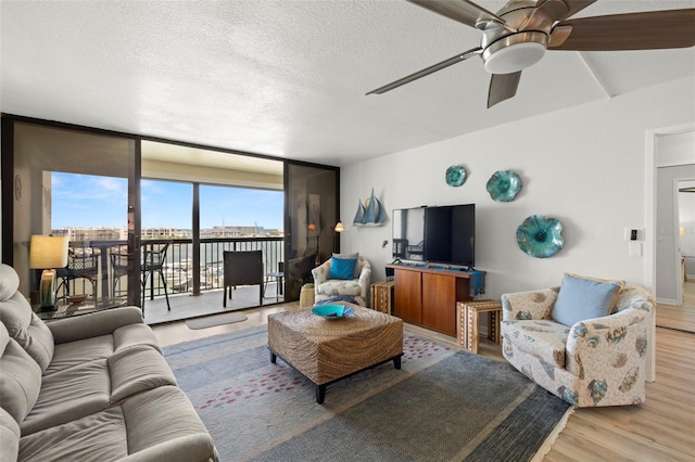 living area with expansive windows, ceiling fan, a textured ceiling, and wood finished floors