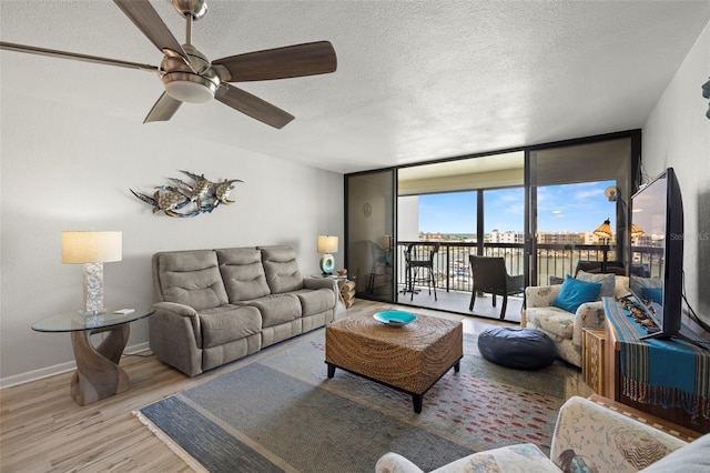 living room with ceiling fan, a textured ceiling, light hardwood / wood-style flooring, and expansive windows