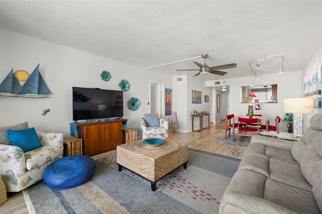 living room featuring ceiling fan, light wood-type flooring, and a textured ceiling