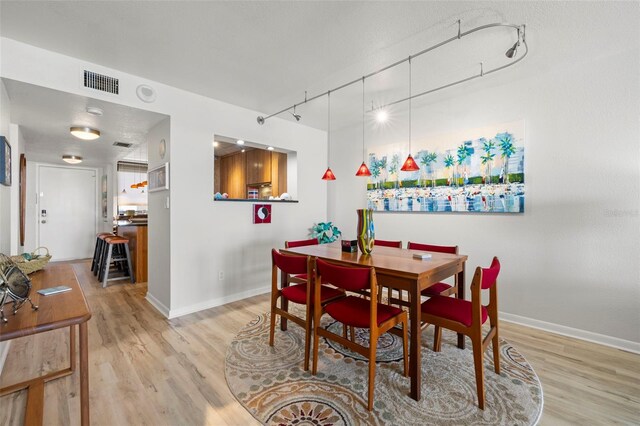 dining area featuring baseboards, rail lighting, visible vents, and light wood-style floors