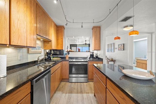 kitchen with stainless steel appliances, dark stone countertops, track lighting, and light hardwood / wood-style flooring