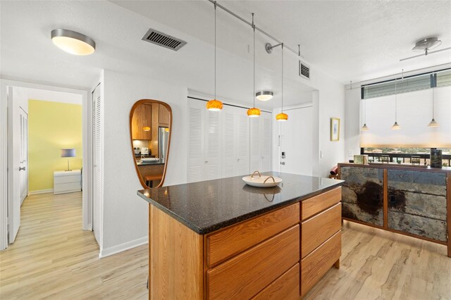 kitchen featuring dark stone counters, decorative light fixtures, light hardwood / wood-style floors, a textured ceiling, and a kitchen island