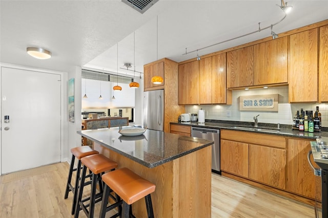 kitchen with visible vents, a sink, stainless steel appliances, light wood-style floors, and backsplash