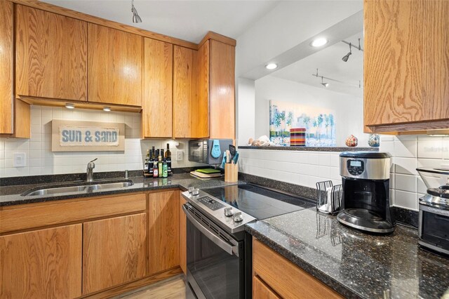 kitchen featuring brown cabinets, stainless steel range with electric stovetop, dark stone counters, and a sink