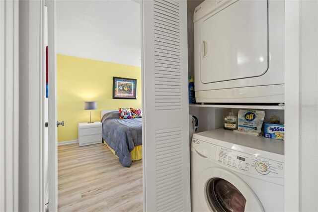 clothes washing area featuring light wood-style floors, stacked washer / drying machine, laundry area, and baseboards