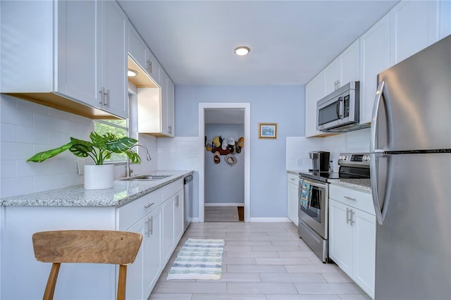 kitchen with decorative backsplash, white cabinetry, light stone counters, sink, and stainless steel appliances