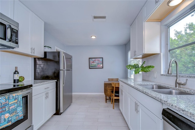 kitchen with appliances with stainless steel finishes, white cabinetry, tasteful backsplash, sink, and light stone countertops