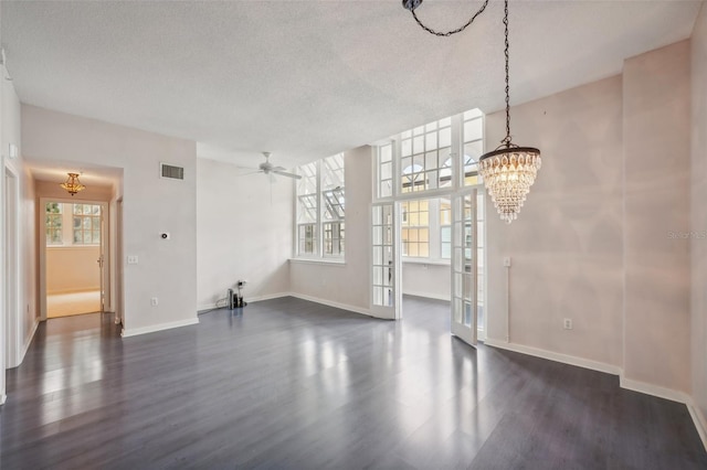 unfurnished dining area featuring a textured ceiling, ceiling fan with notable chandelier, and dark wood-type flooring