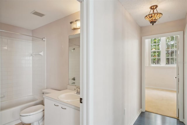 full bathroom with a textured ceiling, vanity, tiled shower / bath combo, and toilet