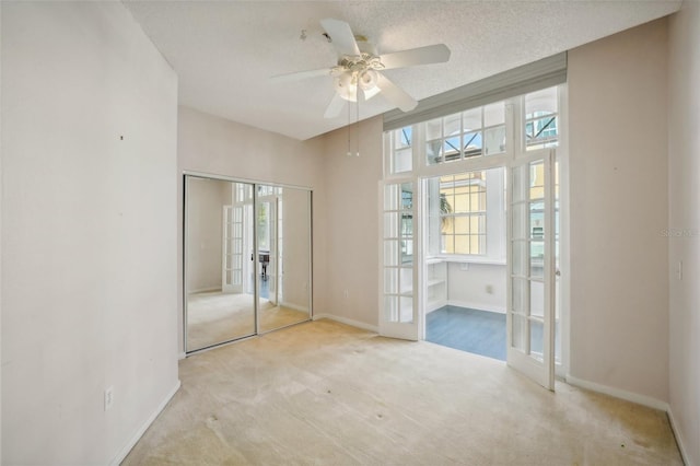 unfurnished bedroom featuring a closet, french doors, a textured ceiling, light carpet, and ceiling fan