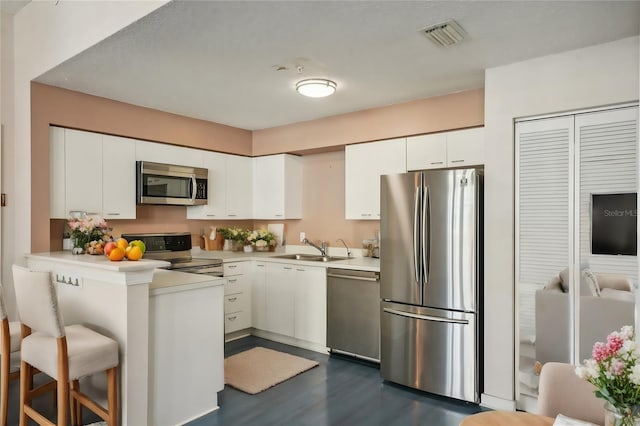 kitchen with stainless steel appliances, white cabinetry, dark hardwood / wood-style floors, sink, and a kitchen breakfast bar