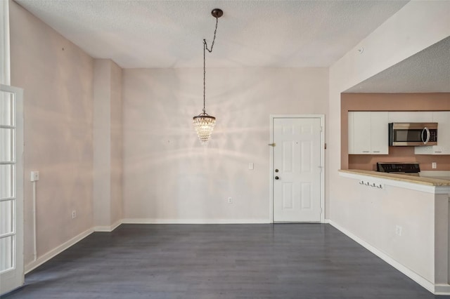 unfurnished dining area with a textured ceiling, dark wood-type flooring, and a chandelier