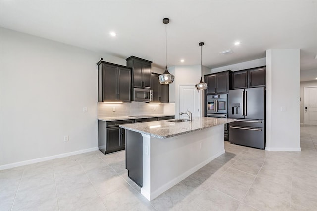 kitchen with a kitchen island with sink, light tile patterned floors, decorative light fixtures, decorative backsplash, and appliances with stainless steel finishes