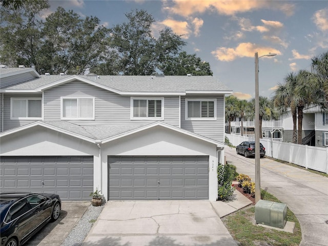 view of property featuring a shingled roof, concrete driveway, fence, and an attached garage