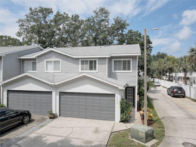 view of front facade featuring a garage, fence, concrete driveway, roof with shingles, and stucco siding