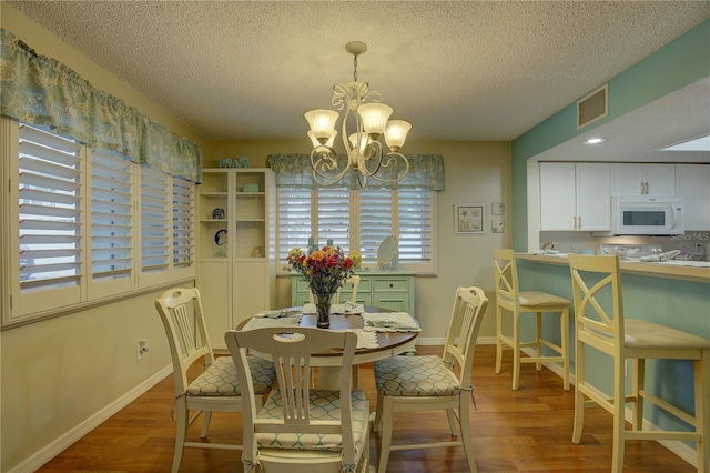 dining space with hardwood / wood-style flooring, a textured ceiling, and a chandelier