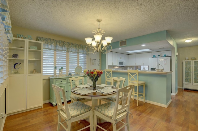 dining area featuring light wood-type flooring, an inviting chandelier, and a textured ceiling