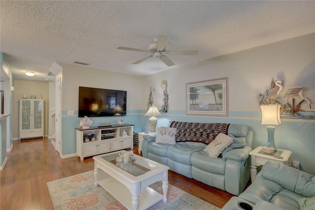 living room with light hardwood / wood-style floors, ceiling fan, and a textured ceiling