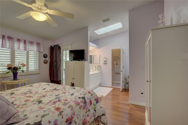 bedroom with light wood finished floors, vaulted ceiling with skylight, visible vents, ceiling fan, and a textured ceiling