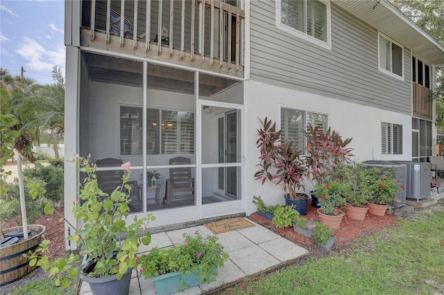 rear view of property featuring a balcony, a sunroom, cooling unit, and stucco siding