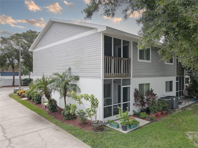 view of home's exterior featuring cooling unit, a sunroom, a lawn, and stucco siding