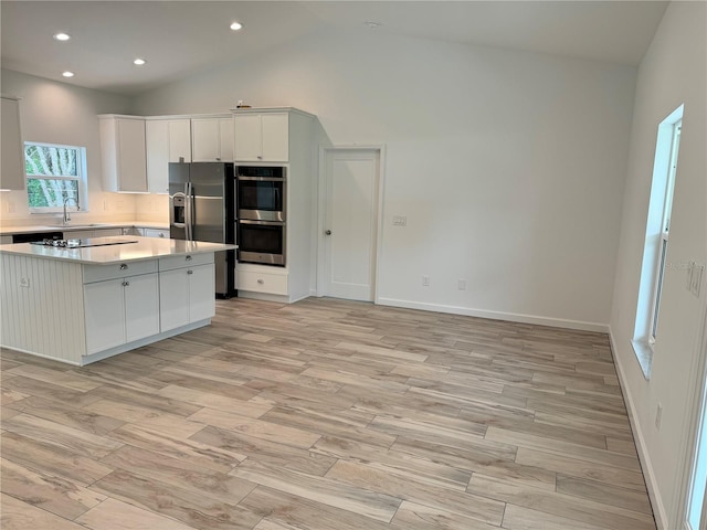 kitchen featuring high vaulted ceiling, white cabinetry, light hardwood / wood-style floors, sink, and stainless steel appliances