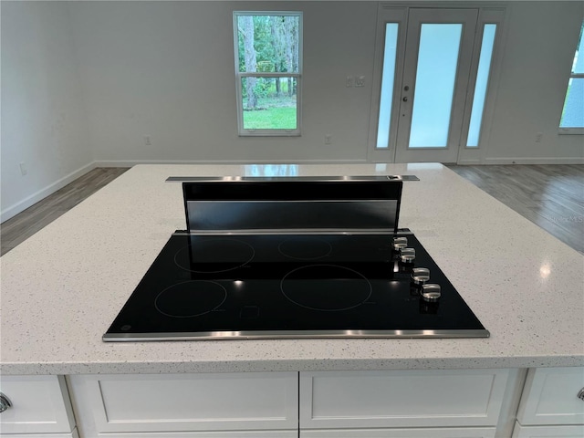 details with hardwood / wood-style flooring, cooktop, white cabinetry, and light stone countertops