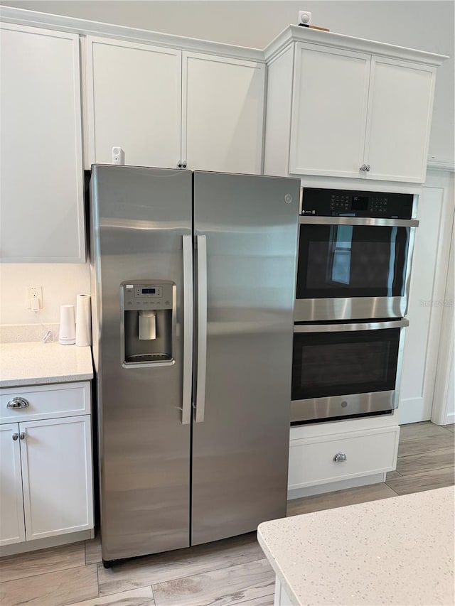 kitchen featuring light wood-type flooring, white cabinetry, appliances with stainless steel finishes, and light stone counters