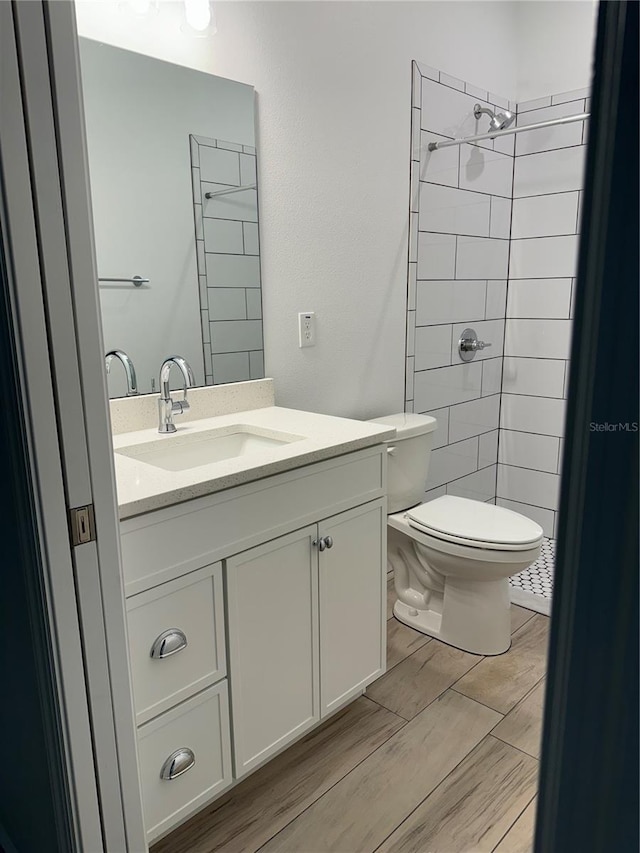 bathroom with toilet, a tile shower, vanity, and hardwood / wood-style floors