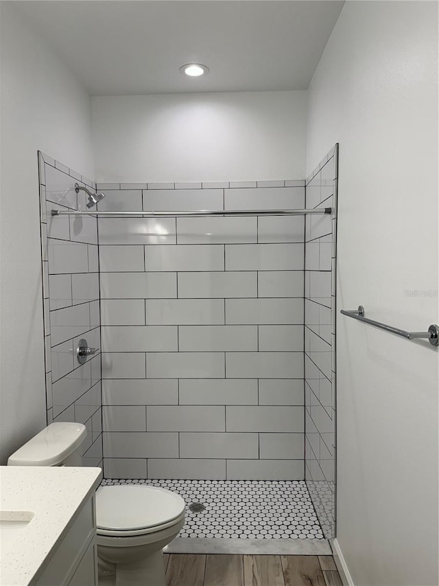 bathroom featuring wood-type flooring, vanity, tiled shower, and toilet