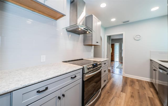 kitchen featuring stainless steel appliances, wall chimney exhaust hood, and light hardwood / wood-style flooring