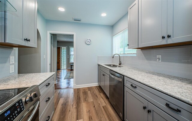 kitchen featuring sink, light hardwood / wood-style flooring, decorative backsplash, light stone countertops, and stainless steel appliances