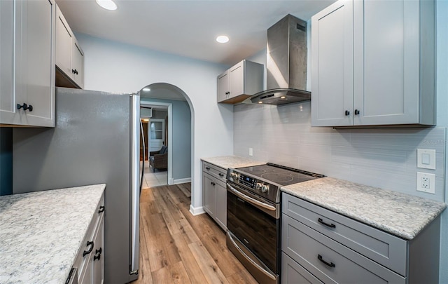 kitchen featuring light hardwood / wood-style flooring, backsplash, wall chimney exhaust hood, gray cabinetry, and appliances with stainless steel finishes