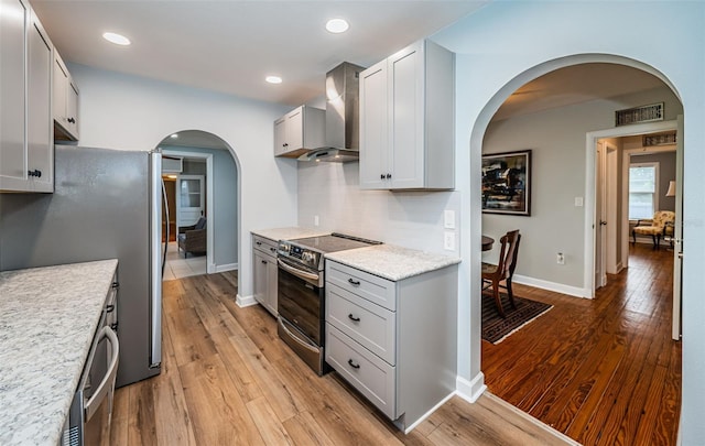 kitchen featuring light wood-type flooring, electric range, gray cabinets, wall chimney exhaust hood, and stainless steel refrigerator