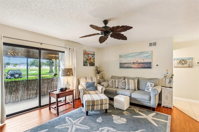 living area with visible vents, a ceiling fan, a textured ceiling, wood finished floors, and baseboards