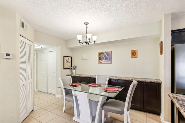 dining space featuring visible vents, a textured ceiling, an inviting chandelier, and light tile patterned floors