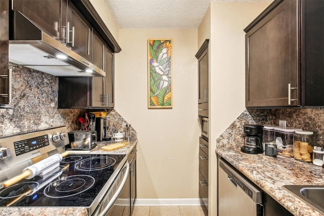 kitchen with decorative backsplash, light stone countertops, stainless steel appliances, dark brown cabinets, and under cabinet range hood