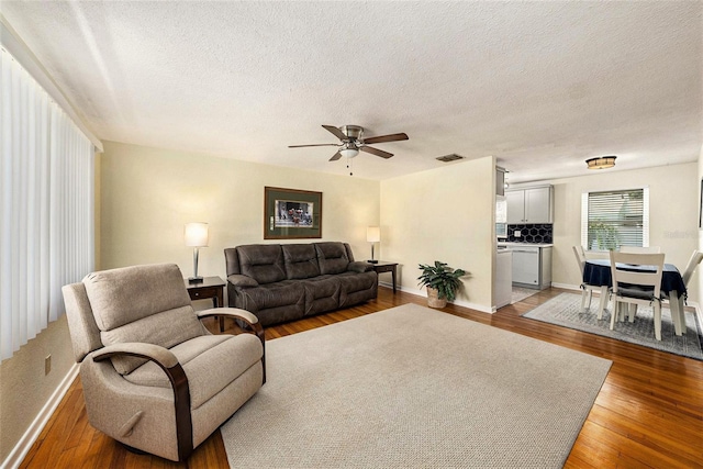 living room with a textured ceiling, ceiling fan, and wood-type flooring