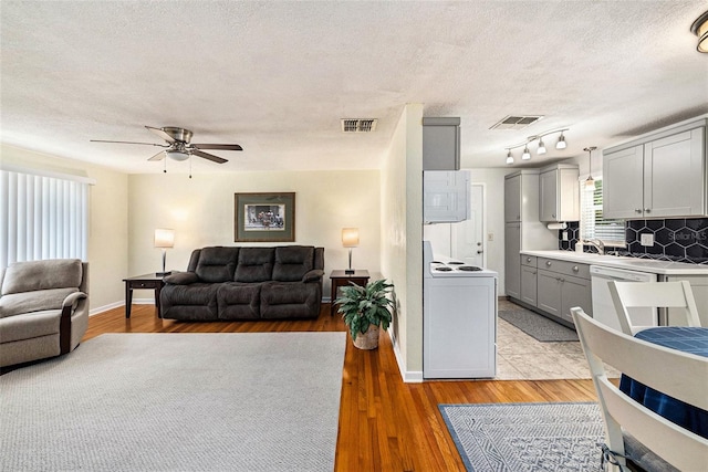 living room featuring ceiling fan, track lighting, a textured ceiling, and light hardwood / wood-style floors