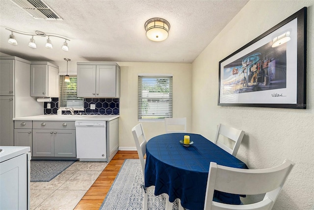 kitchen with rail lighting, plenty of natural light, gray cabinets, and white dishwasher