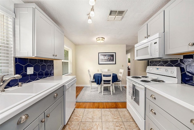 kitchen with backsplash, white appliances, a textured ceiling, and light tile patterned floors