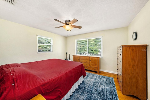 bedroom featuring multiple windows, a textured ceiling, light hardwood / wood-style floors, and ceiling fan