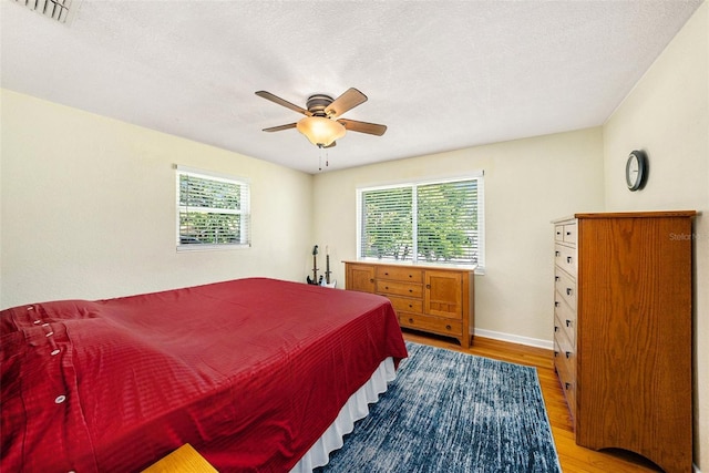 bedroom featuring multiple windows, wood-type flooring, ceiling fan, and a textured ceiling