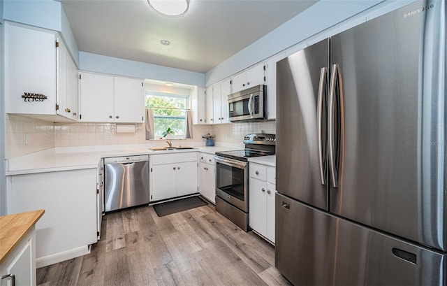 kitchen featuring white cabinets, decorative backsplash, light hardwood / wood-style flooring, and stainless steel appliances