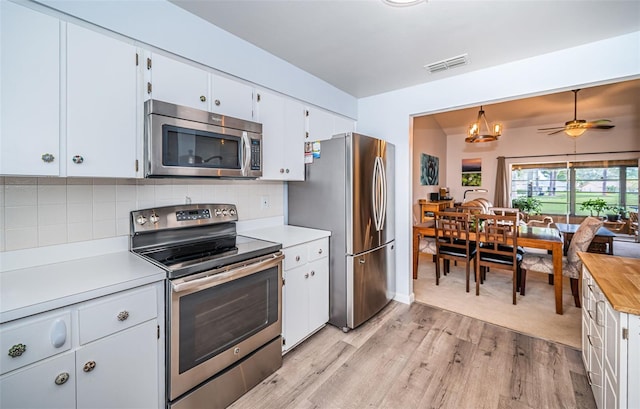 kitchen featuring appliances with stainless steel finishes, decorative backsplash, white cabinets, light colored carpet, and hanging light fixtures