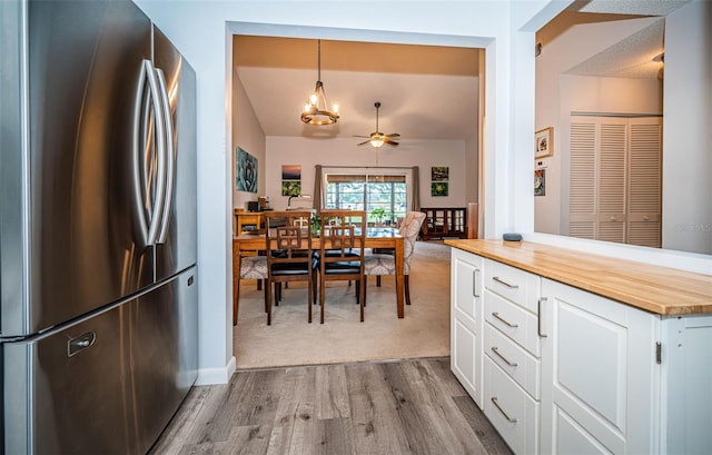 kitchen with wooden counters, light colored carpet, white cabinetry, decorative light fixtures, and stainless steel fridge