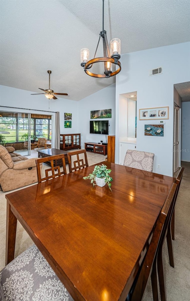 dining space featuring carpet floors, ceiling fan with notable chandelier, a textured ceiling, and lofted ceiling