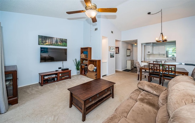 carpeted living room with ceiling fan with notable chandelier, high vaulted ceiling, and sink